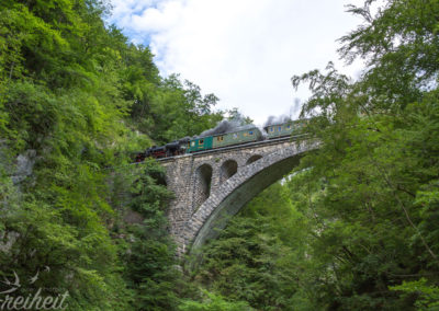 Über dem Damm rauscht eine Dampfeisenbahn hinweg